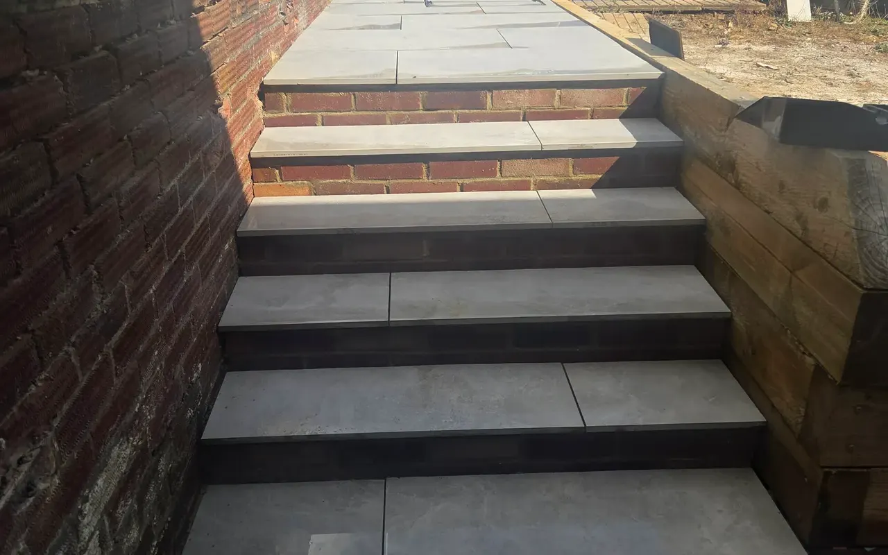 Grey paving on steps with brick risers, a brick wall and timber edging
