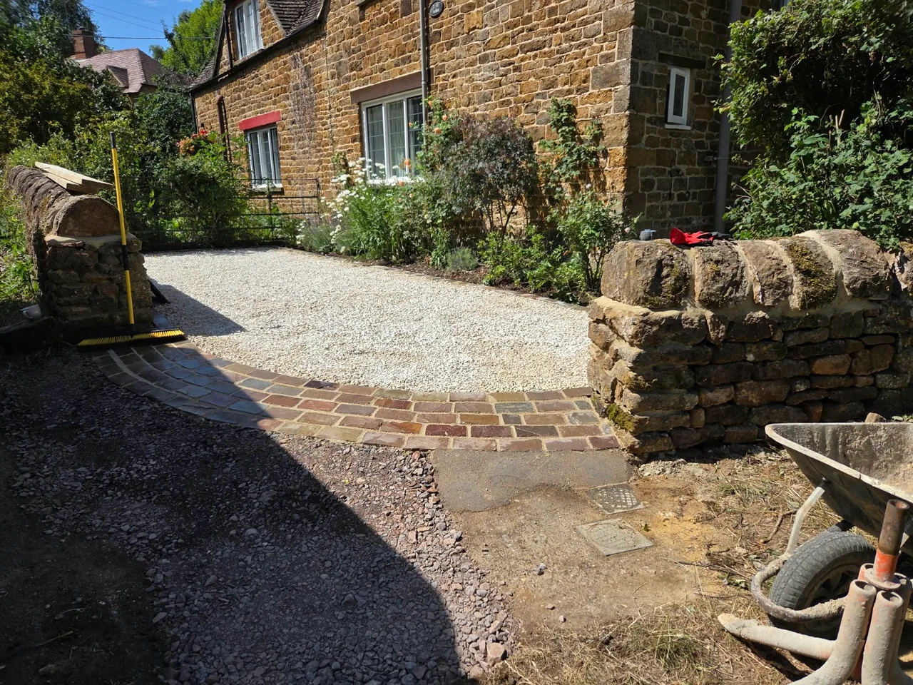 Light gravel entrance with curved paved edging between stone walls in Banbury