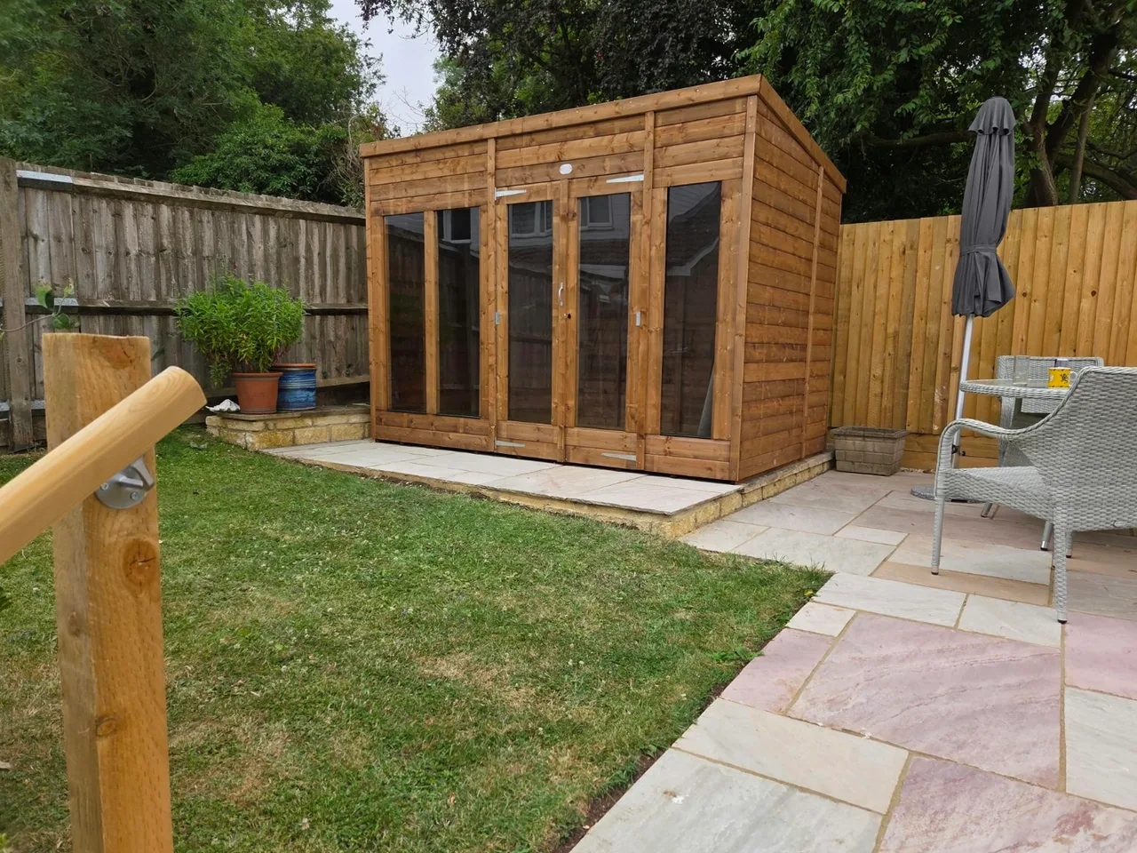 Timber summerhouse with glazed doors and paving beside a lawn in Chipping Norton