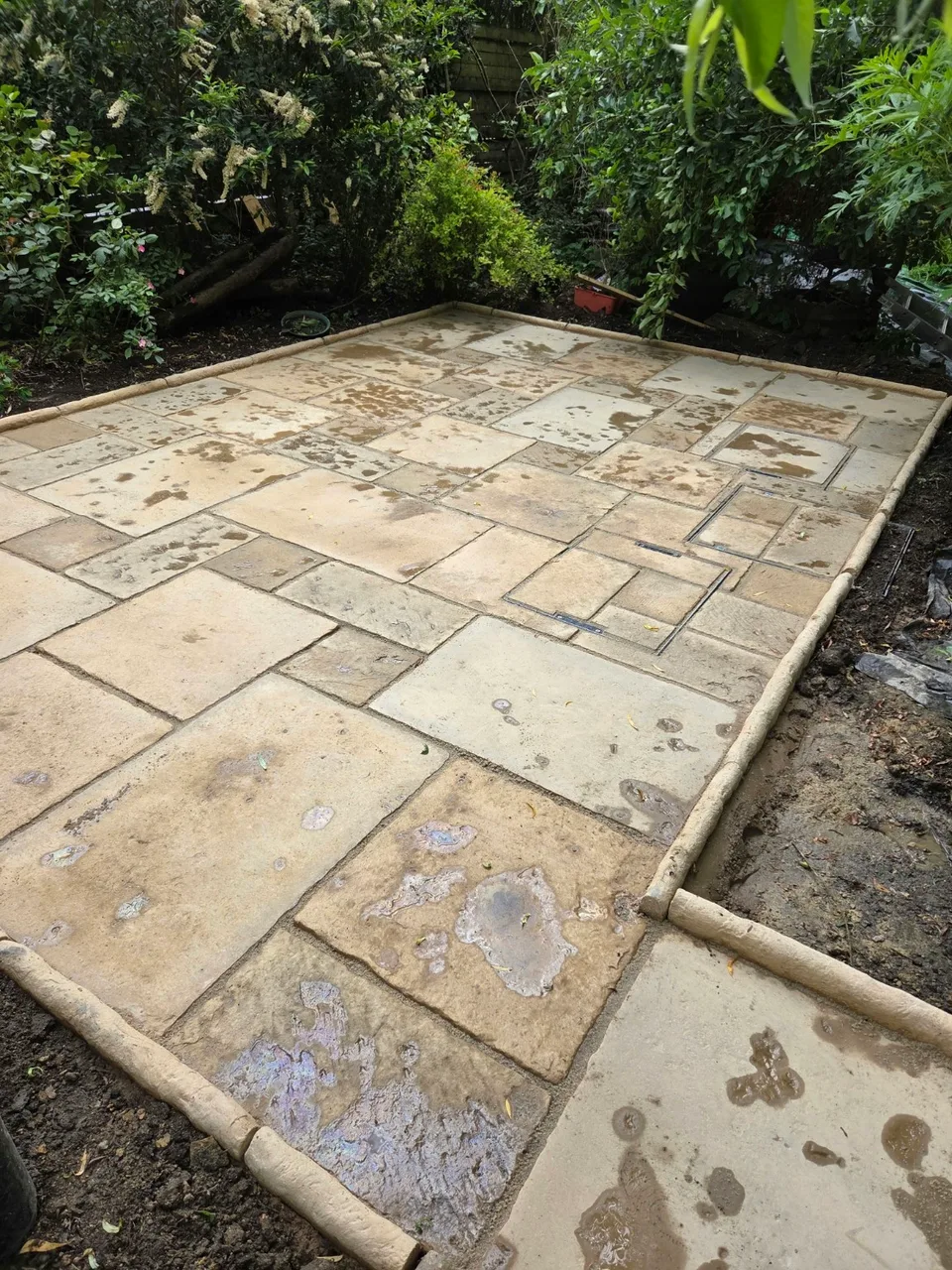 Garden patio with varied slab sizes, perimeter edging and two inset access covers in Enstone
