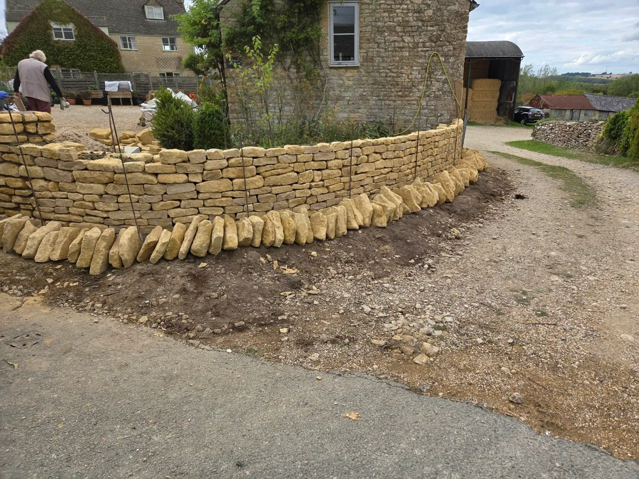 Curved stone wall being built in Nether Westcote, with coping stones laid out in front