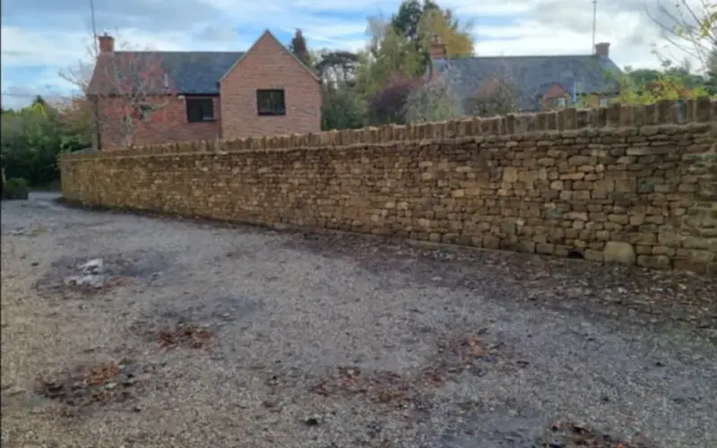 Long natural stone boundary wall with upright coping beside a gravel area